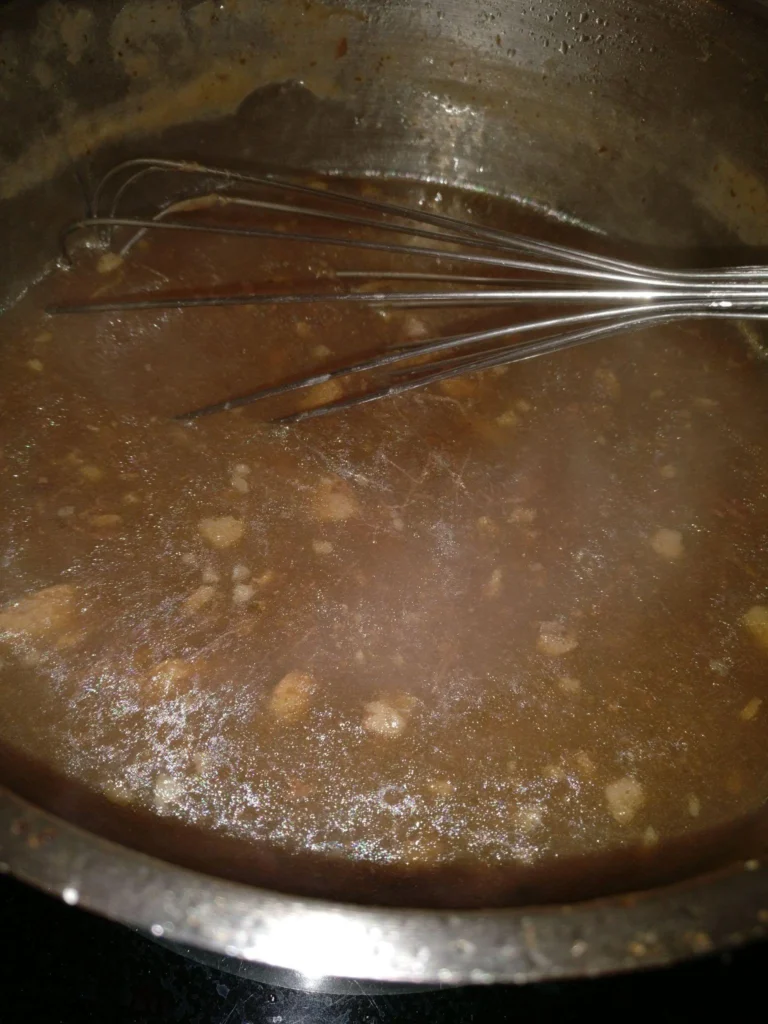 Homemade beef gravy being stirred in a saucepan after cooking slow cooker pot roast