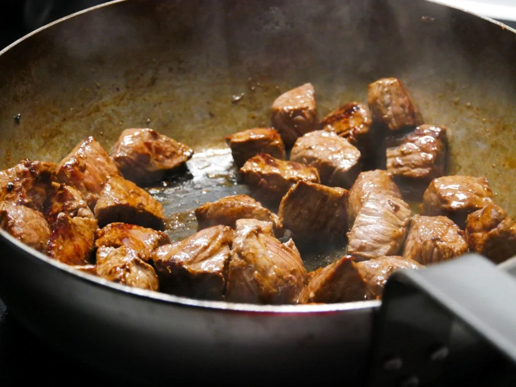 Browning beef cubes in a hot skillet before adding them to a slow cooker for beef tips recipe