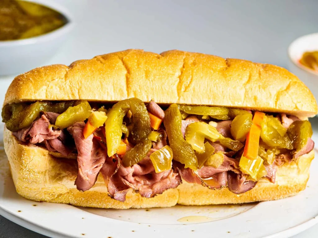 Italian beef recipe slow cooker sandwich with shredded beef, pepperoncini, and melted provolone on a toasted hoagie roll